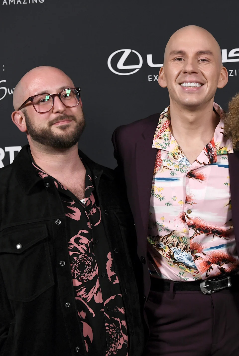 Three individuals pose on the red carpet at the Queerties event, dressed in patterned shirts and formal jackets, radiating happiness and pride
