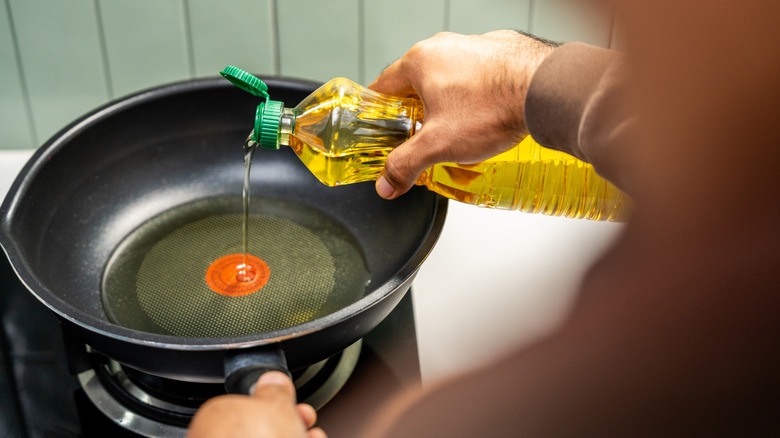 Person pouring vegetable oil into skillet