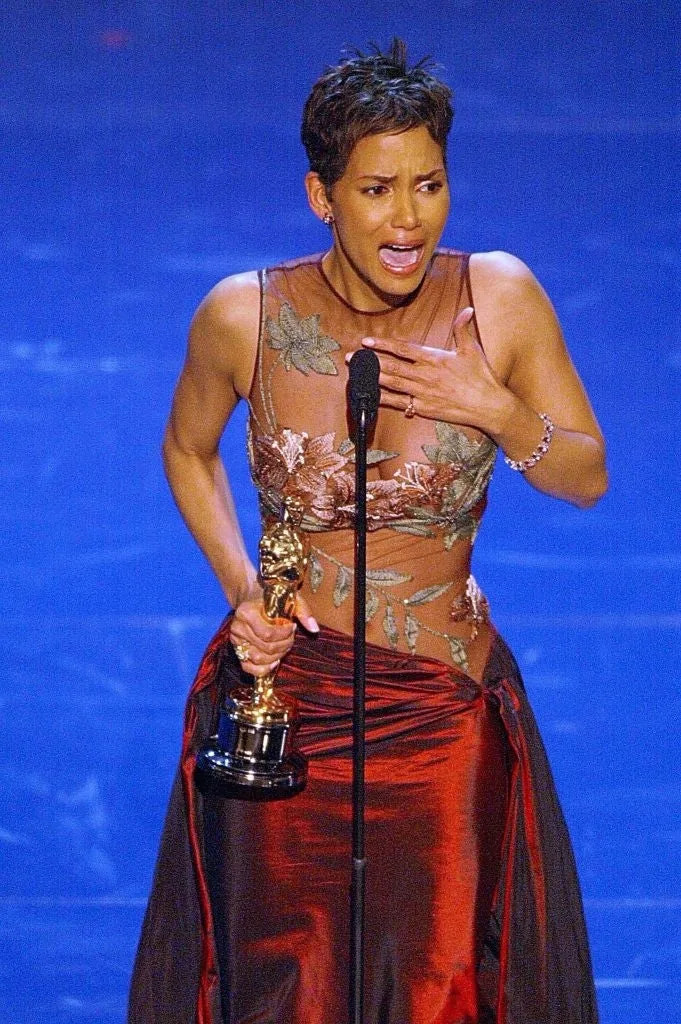 Halle Berry in an elegant gown, emotional, holding an award and speaking at a microphone on stage