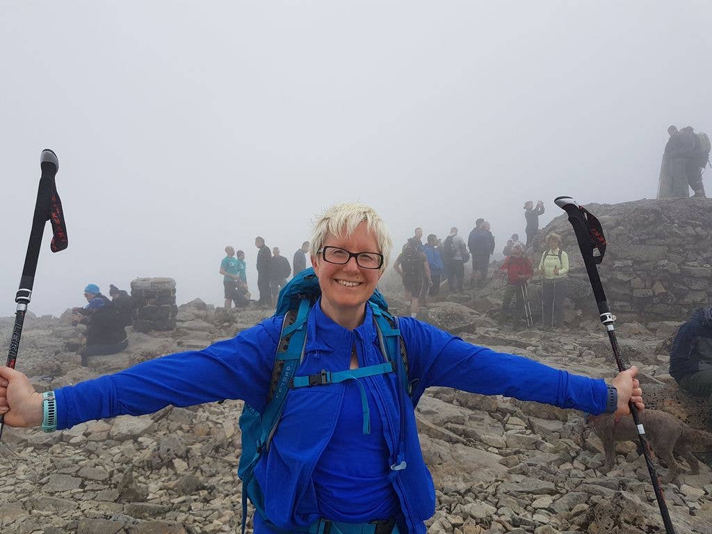 Woman in blue at the top of a mountain with walking poles