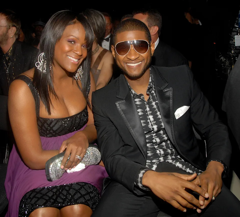 Two people smiling at an event, one in a patterned shirt with a suit, and the other in a strapless dress with sparkling accessories