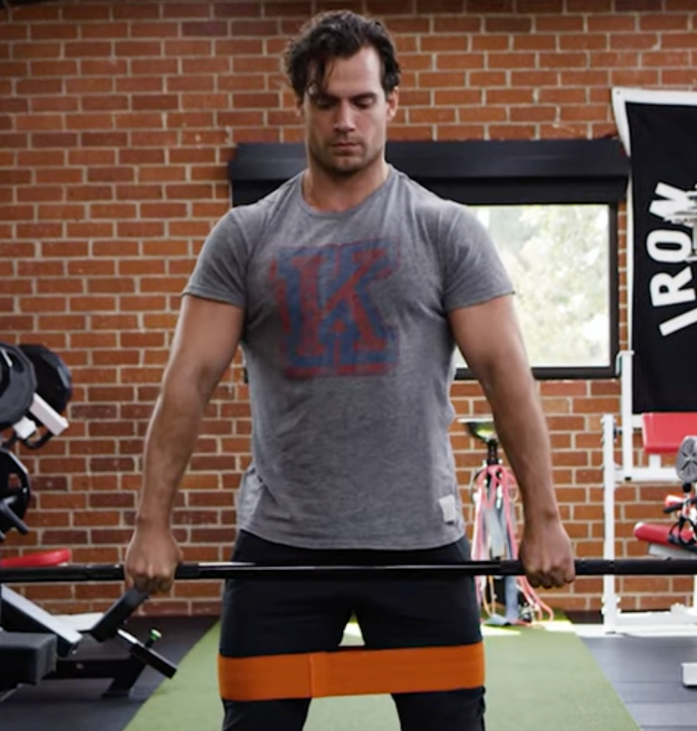 individual performing resistance training with a barbell and resistance band in a gym