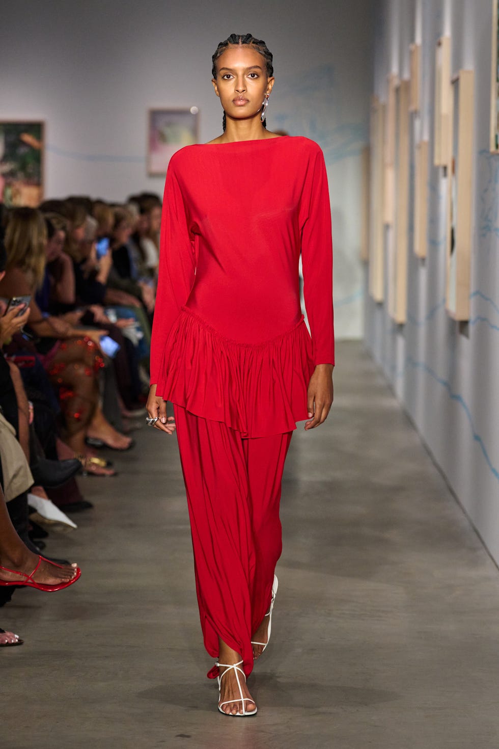 Model walking down the runway in a flowing red outfit at a fashion show.