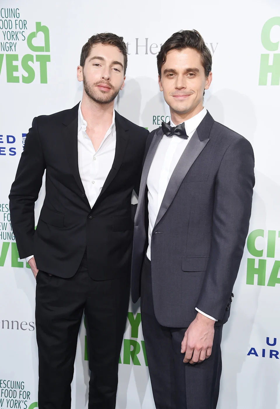 Two people posing on a red carpet event. Both wear suits; the person on the right also wears a bow tie