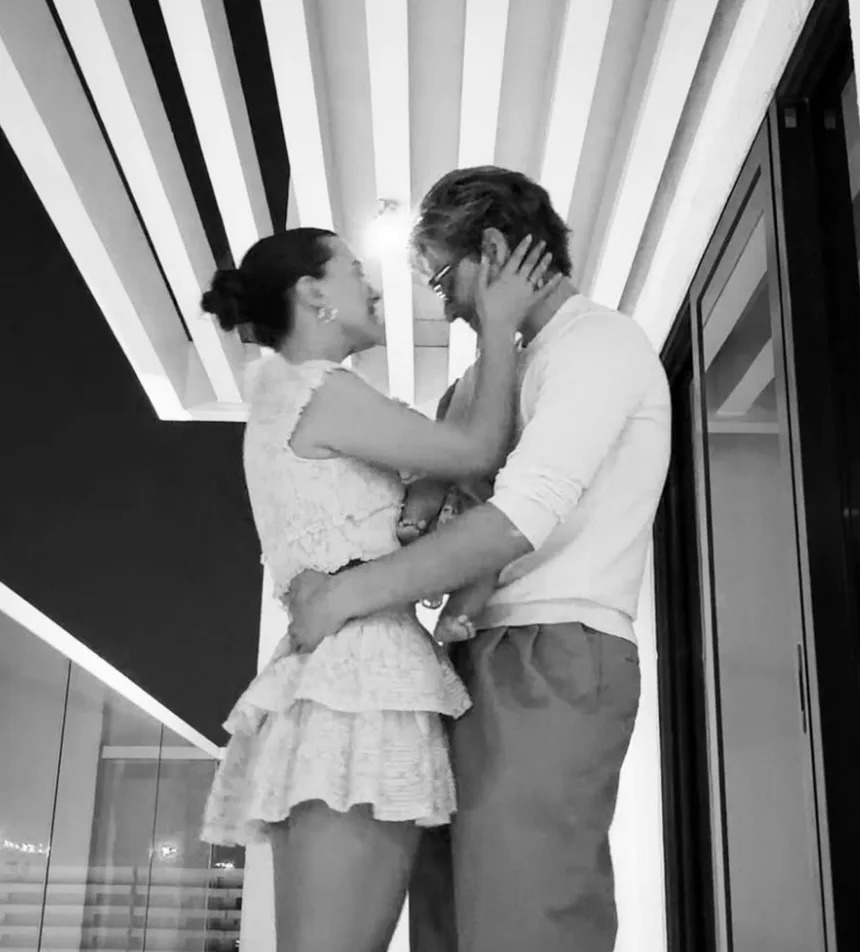 A couple in elegant attire embraces in a modern, stylish setting with geometric ceiling patterns