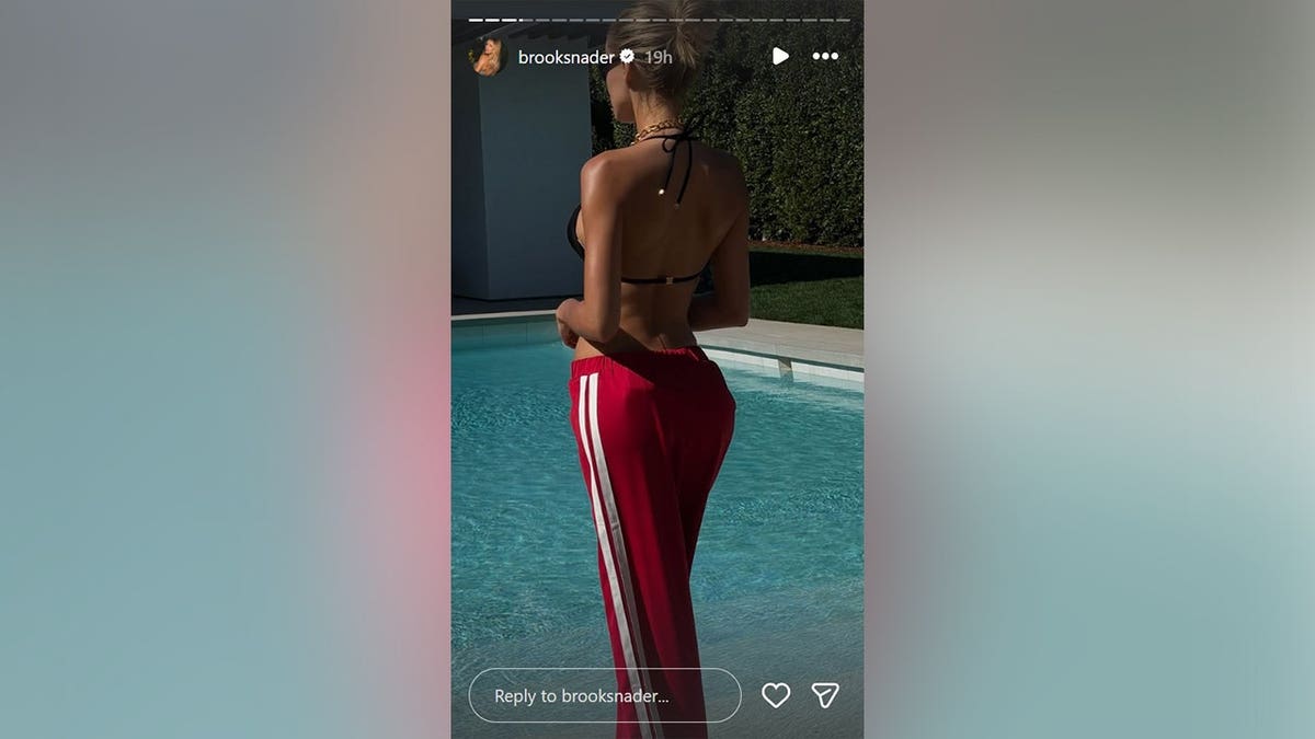 Brooks Nader standing next to a swimming pool in a black bikini.