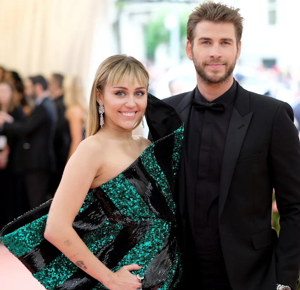 A celebrity couple poses at an event. She wears a shimmering, structured gown, and he is in a classic tuxedo