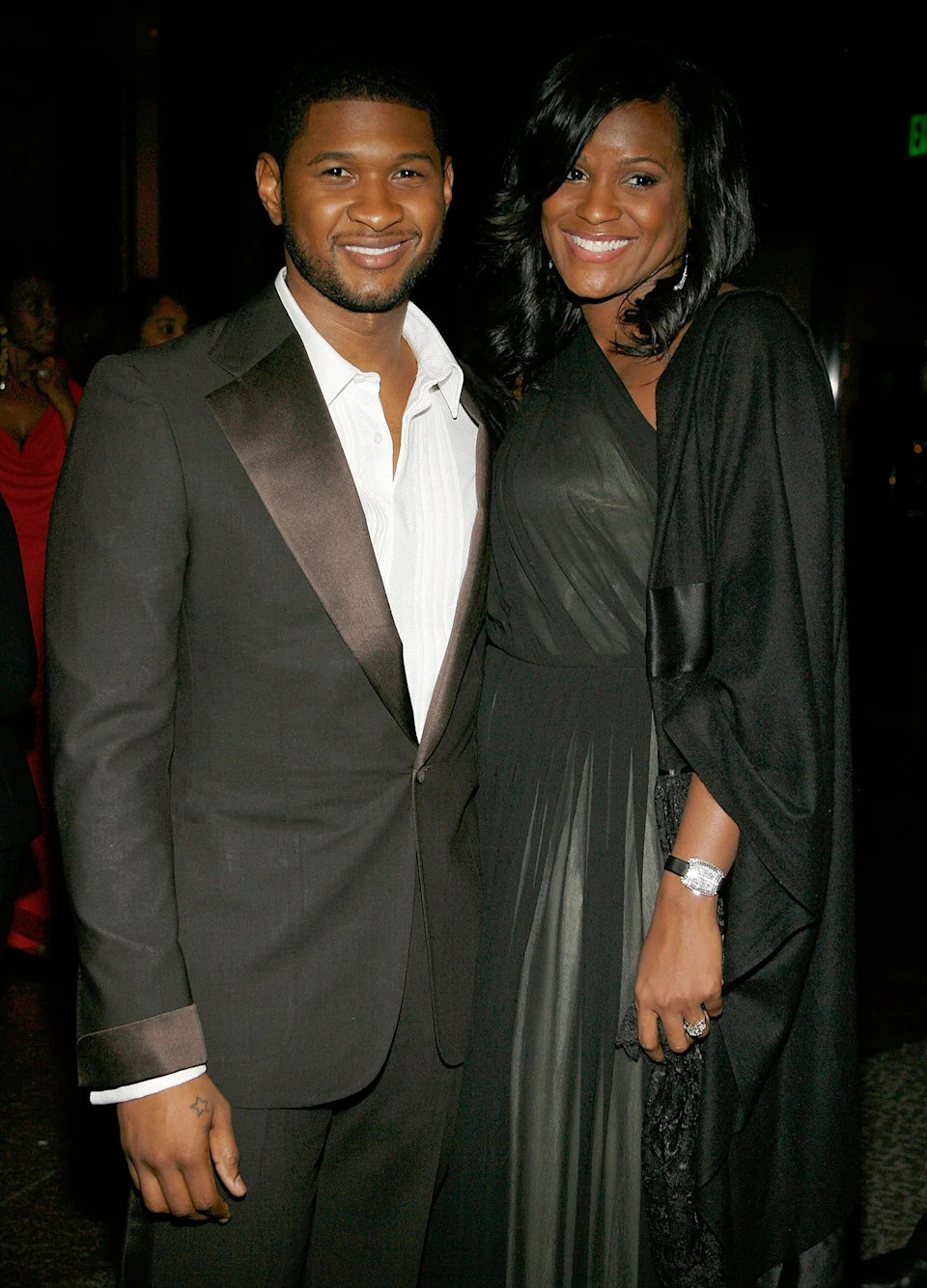 A man in a tailored suit poses with a woman in an elegant gown at a formal event, both smiling at the camera