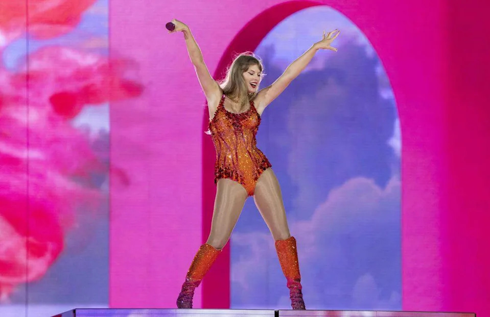 Performer on stage in a sparkling outfit with microphone, striking an energetic pose against a vibrant, colorful backdrop