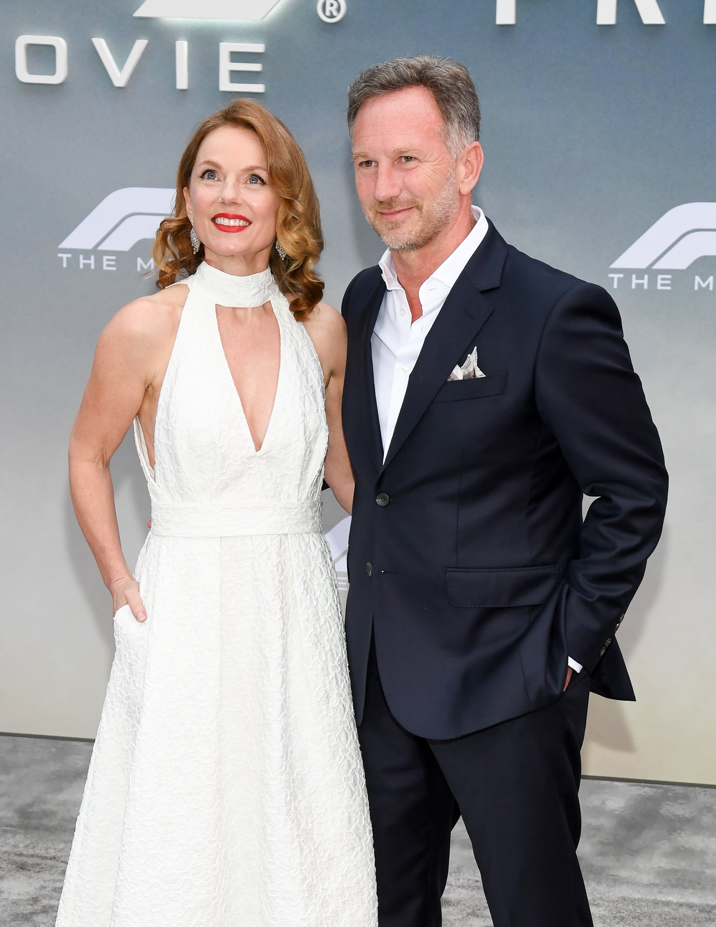 A couple posing at a formal event. The woman wears a white halter dress, and the man is in a dark suit with a pocket square