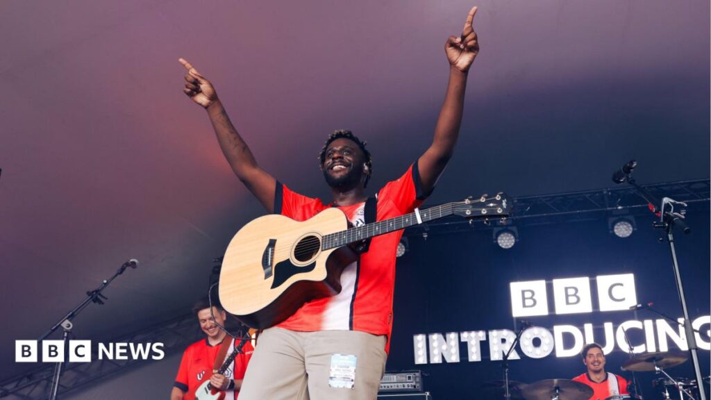 Myles Smith announces surprise Luton show ahead of album release Myles Smith performing at Radio 1's Big Weekend in 2024. He has his arms in the air and is looking out towards the crowd with his guitar round his neck. There is an illuminated BBC Introducing sign behind him.