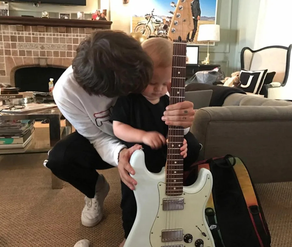 Person in casual clothing helps a child hold an electric guitar in a cozy living room