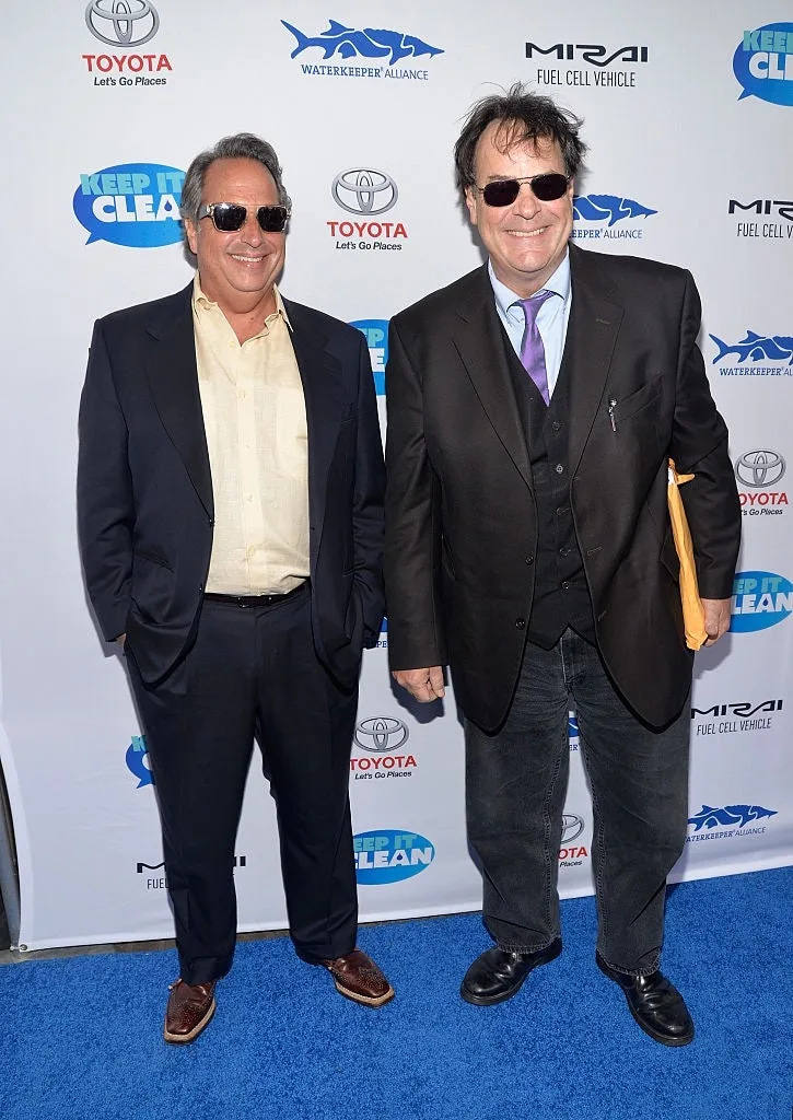 Two people in sunglasses on a blue carpet at a "Keep It Clean" event, wearing suits