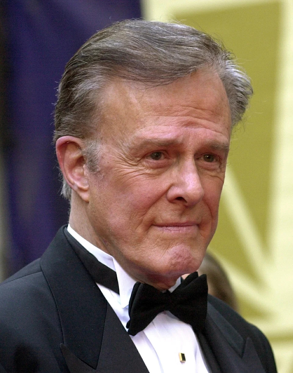 Man in a tuxedo with a bow tie, looking ahead thoughtfully at a formal event