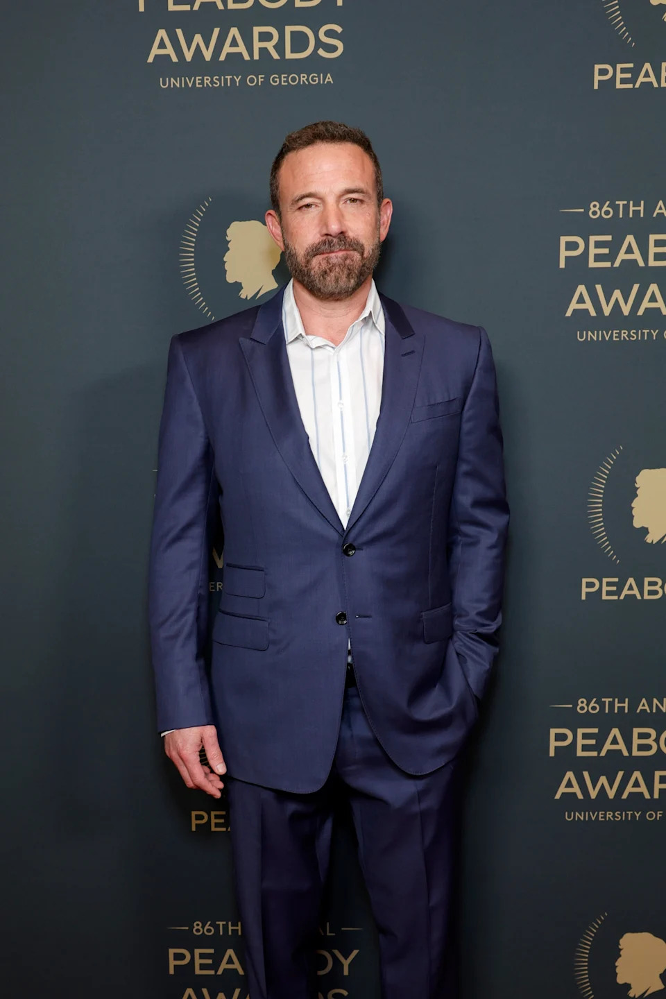 Man in a suit stands on a red carpet at the Peabody Awards event backdrop