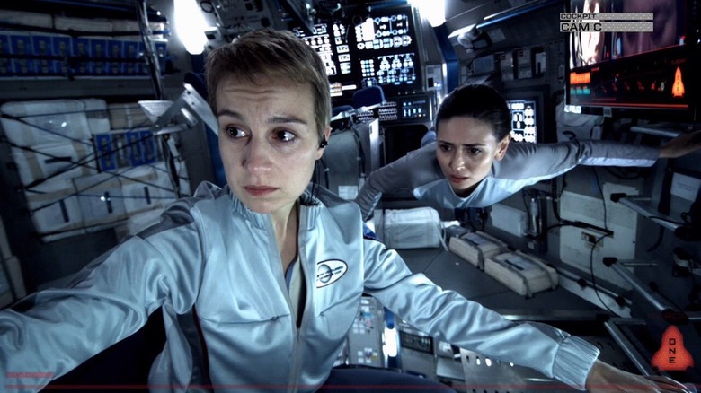 Anamaria Marinca as Rosa Dasque and Karolina Wydra as Katya Petrovna in Europa Report, in the bay of a ship, as Rosa sits and looks over at something and Katya floats in zero-gravity and looks the same direction.