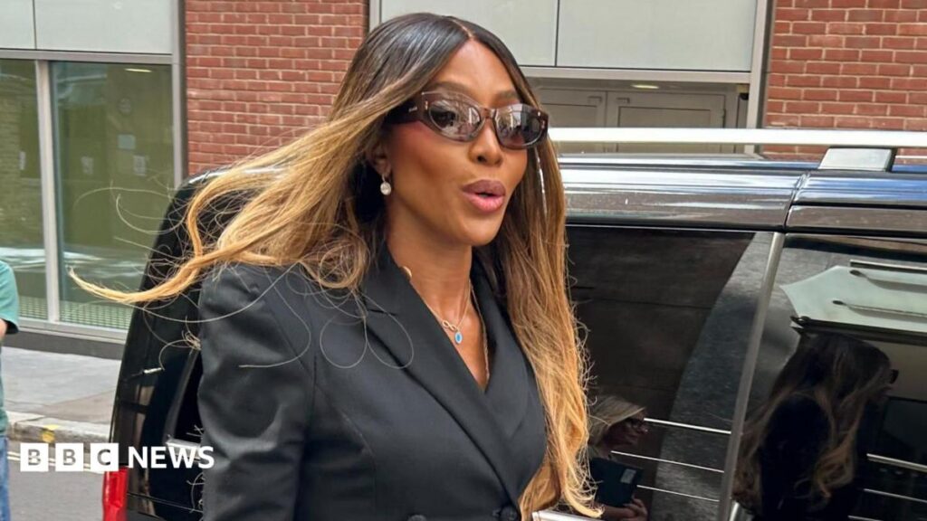 Naomi Campbell blames lawyer for ‘fraud and deception’ at charity ban appeal Naomi Campbell has long blonde and brown straight hair, brown sunglasses and a black blazer jacket. She is walking along, having just got out of a black car.
