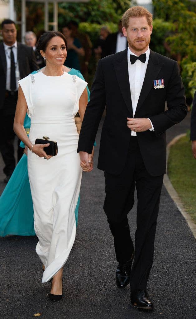 The Duchess of Sussex in a white dress holding hands with Prince Harry