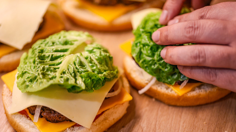 Hands assembling cheeseburgers with lettuce