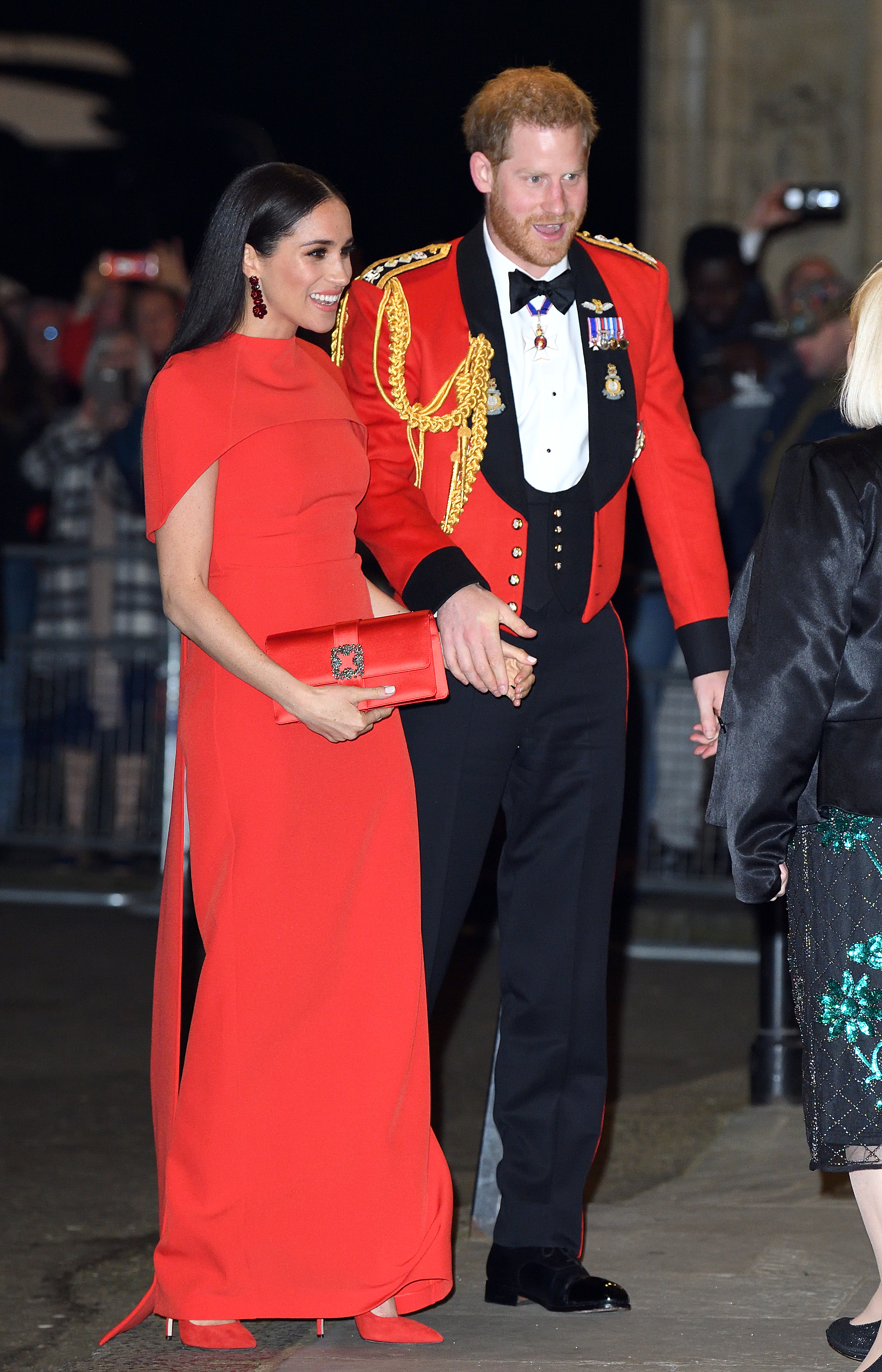Meghan Markle wearing a red gown and Prince Harry wearing a red uniform