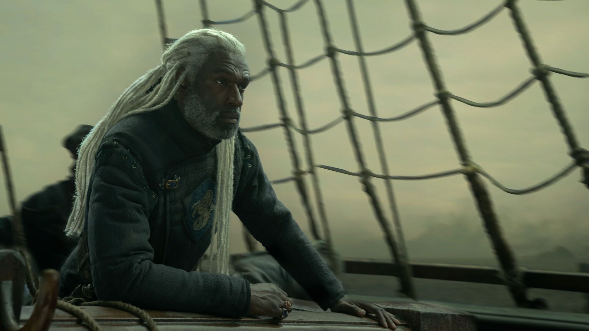 A man with long white hair sits on a ship.