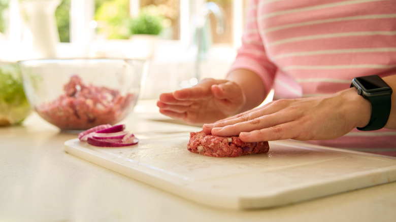 Person shaping burger patty with hands on cutting board
