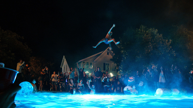 A bunch of high-schoolers hanging around a lit-up pool at night in Project X, cheering on a peer jumping into the pool from very high in the air.