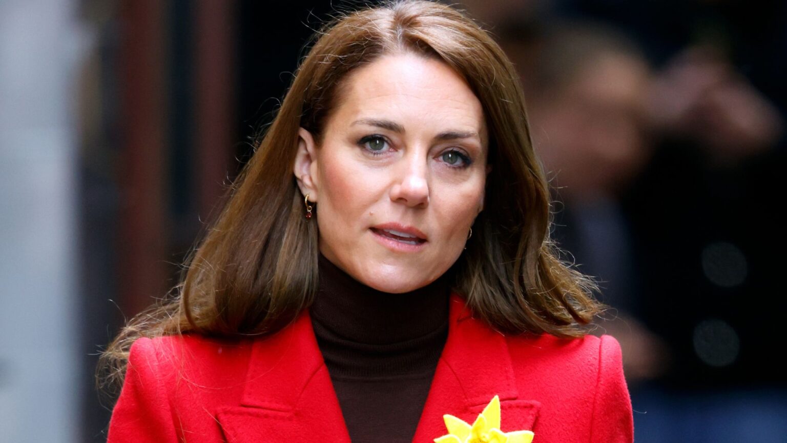 Princess Kate Pushed Back on One Aspect of Royal Family Life Kate Middleton wears a red coat with a black turtleneck sweater and a yellow daffodil on her lapel, she has long brown hair