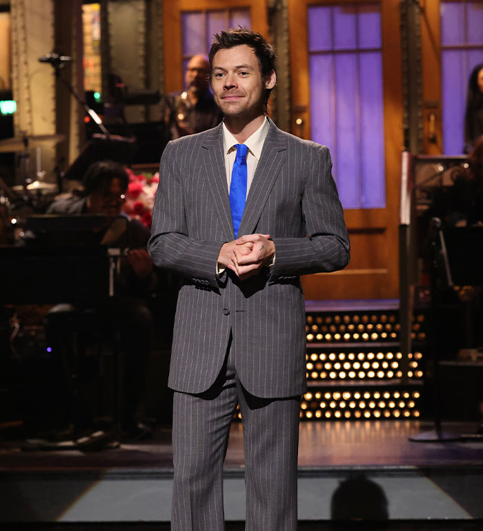 Harry Styles on stage, smiling and clapping, wearing a pinstripe suit, an iconic moment before his wardrobe malfunction. Harry Styles on stage, smiling and clapping, wearing a pinstripe suit, an iconic moment before his wardrobe malfunction.