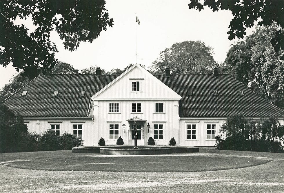 Historic manor house with symmetrical windows and a central entrance surrounded by trees.