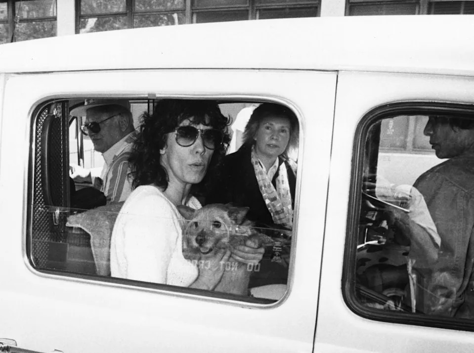Person with sunglasses holding small dog inside a vehicle, accompanied by others. Image relates to an LGBT article