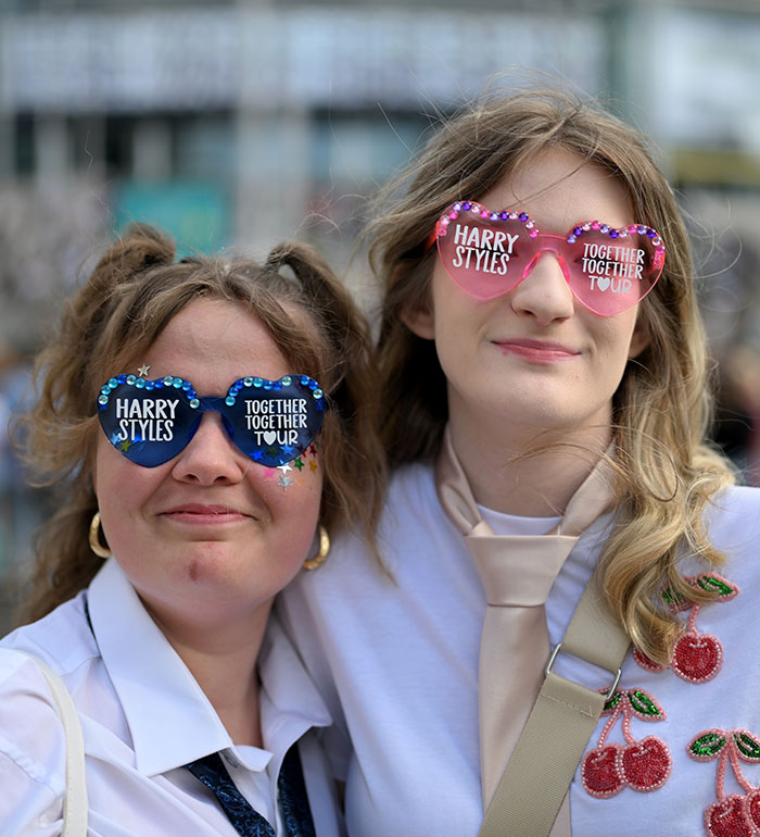 Two fans wearing heart-shaped Harry Styles sunglasses, ready for his concert, after a wardrobe malfunction. Two fans wearing heart-shaped Harry Styles sunglasses, ready for his concert, after a wardrobe malfunction.