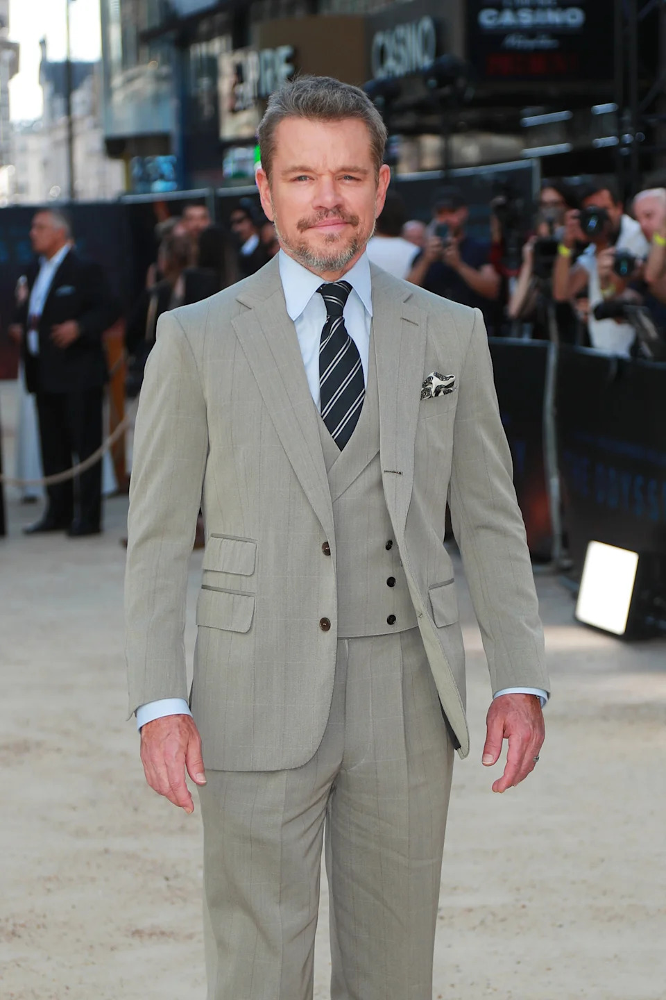 Man in a tailored suit with a patterned tie poses for photos at an event, surrounded by photographers