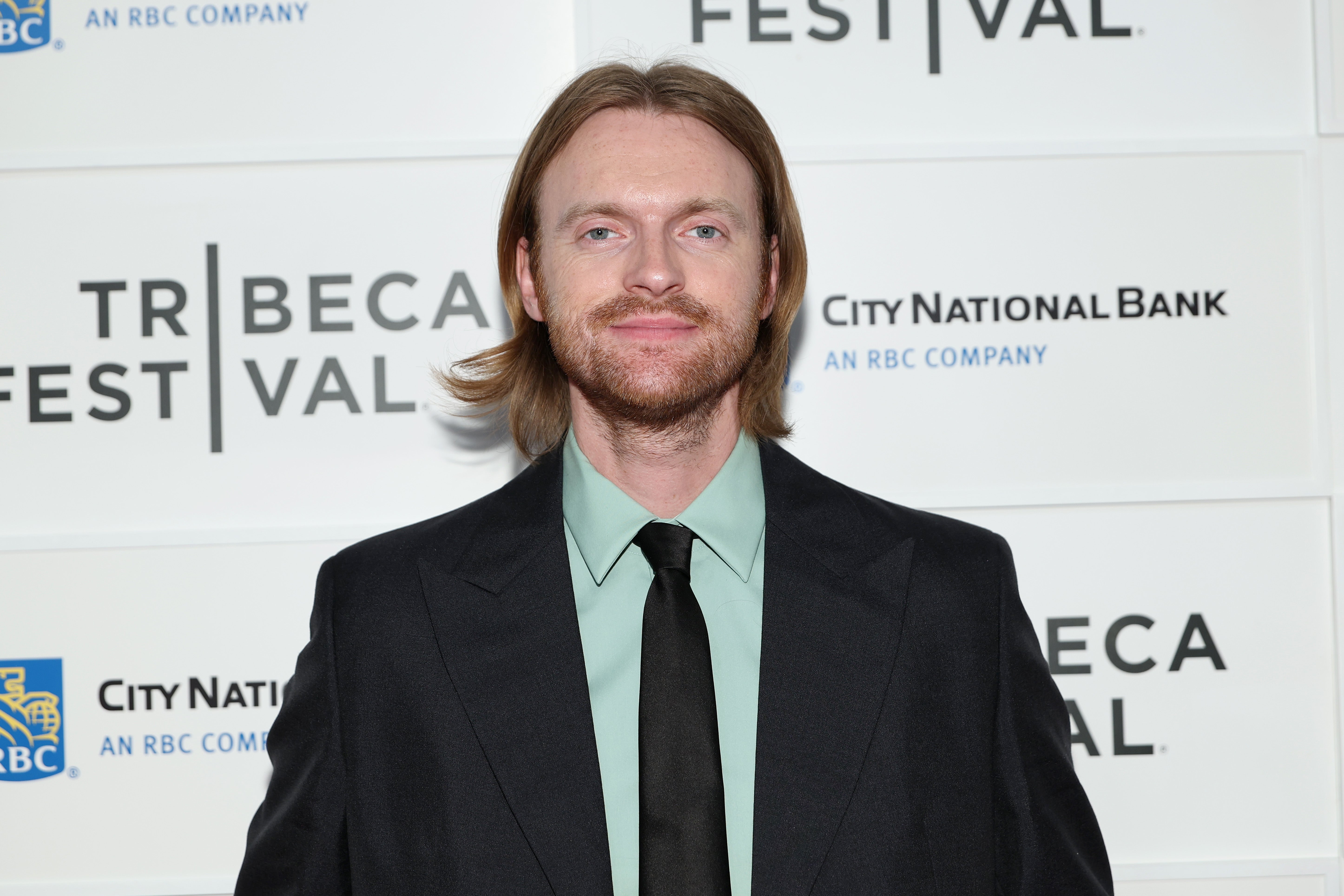 Finneas in a suit on a red carpet at a film festival event backdrop