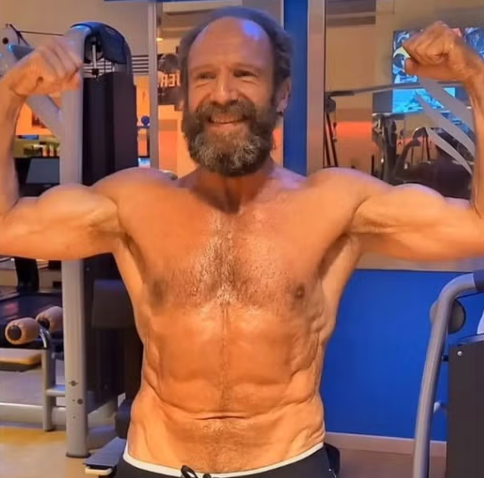 smiling man flexing muscles in a gym.