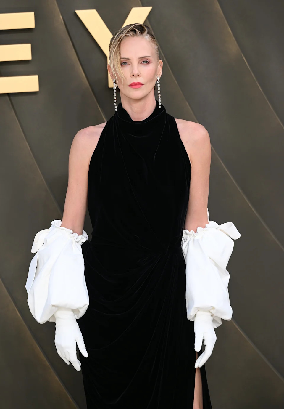 Person in elegant black gown with white gloves and drop earrings, standing at an event