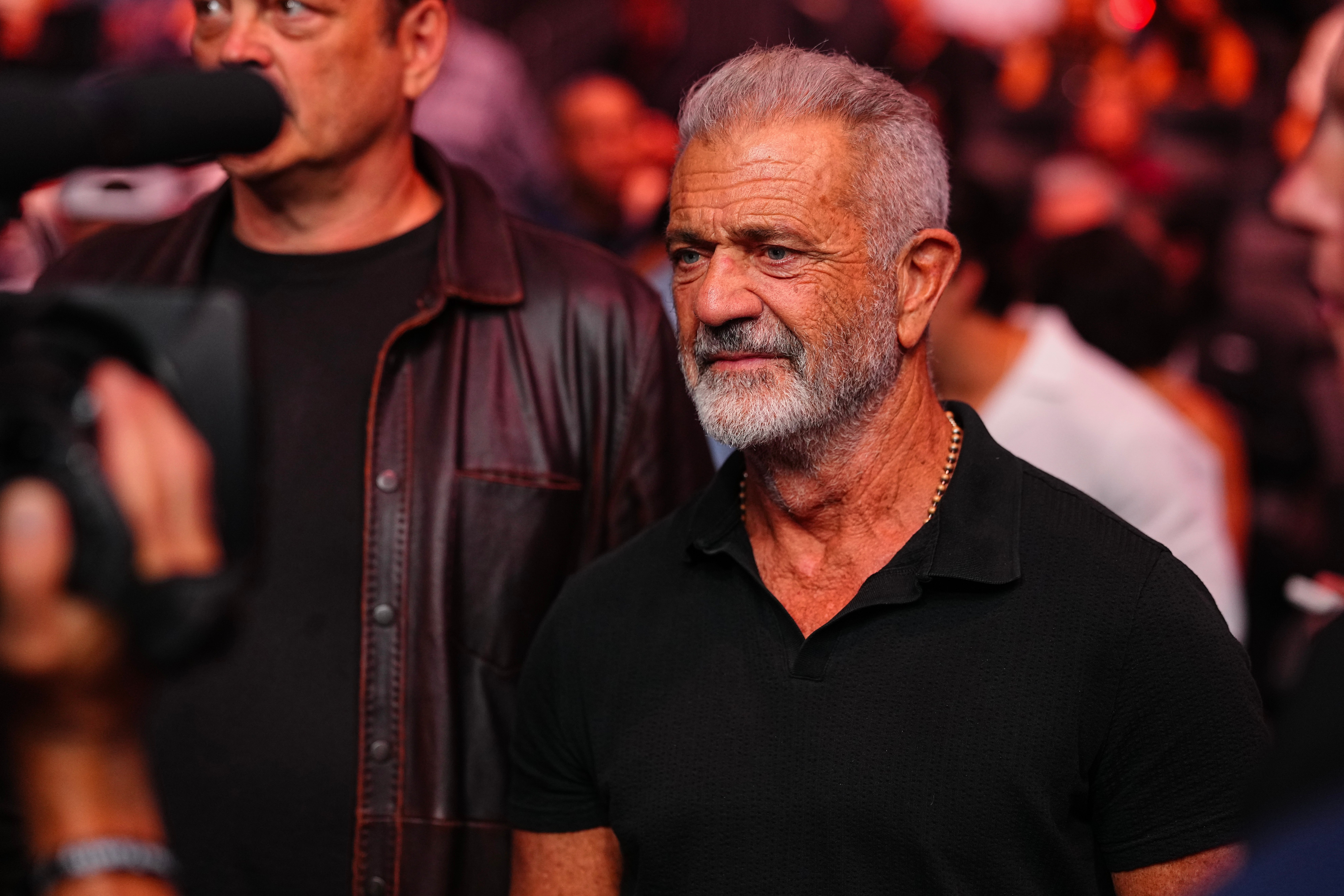Mel Gibson with a beard in a polo shirt is at a crowded event, captured in a candid moment