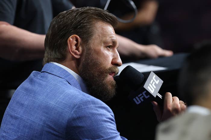 Conor McGregor in a suit speaking into a UFC microphone at an event