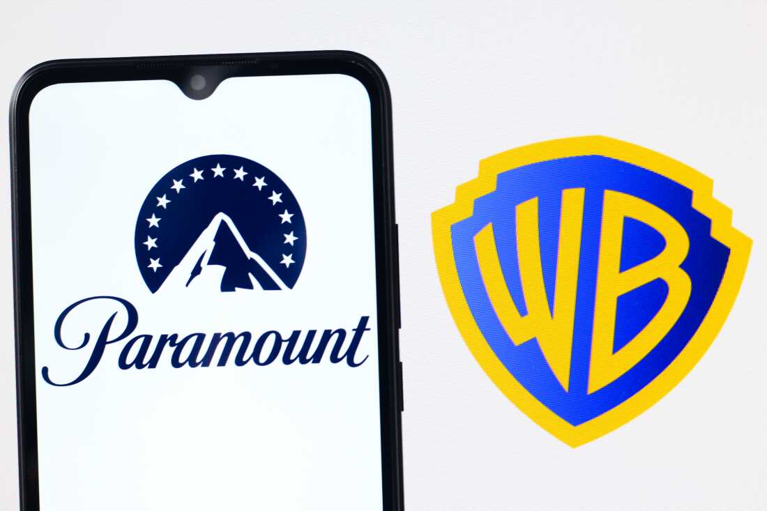 The left side of this image shows a smartphone with Paramount's mountain peak logo on it. The right side shows Warner Bros. Discovery's logo, which has the capital letters W and B in gold on a blue shield.