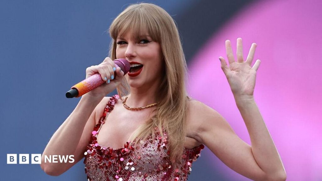 Anfield lost out on ‘global act’ over gig rules, club officials say Close up of Taylor Swift singing at a concert. She has long blonde hair with a fringe and is holding up her left hand wearing a pink sparkly vest