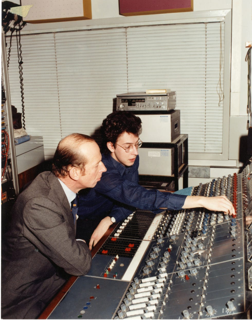 Two men collaborating at a sound mixing console, adjusting sliders and settings in a recording studio environment.
