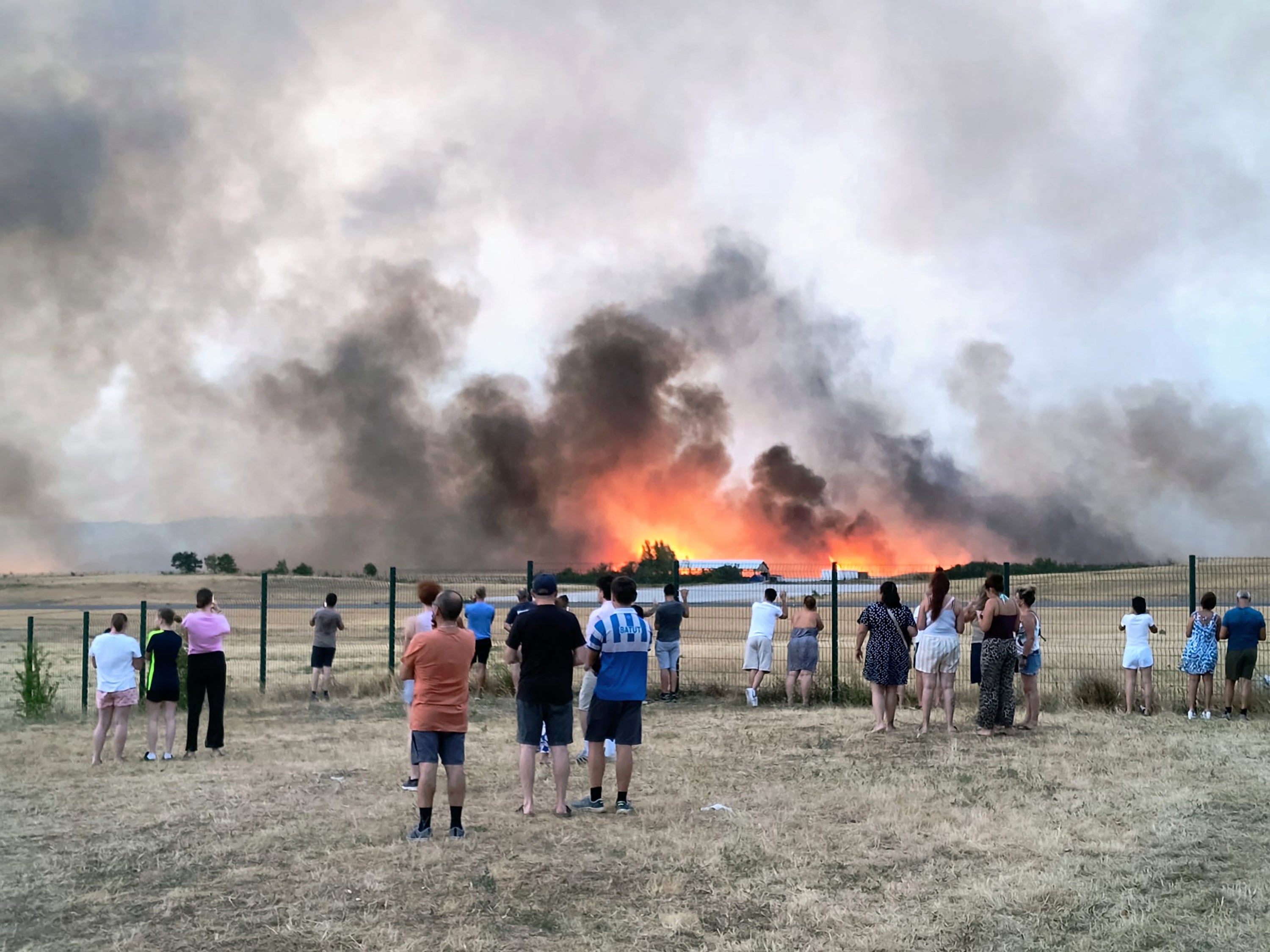 Bystanders look on as fire and smoke billow across Castres-Mazamet aerodrome, near Labruguiere in south-western France