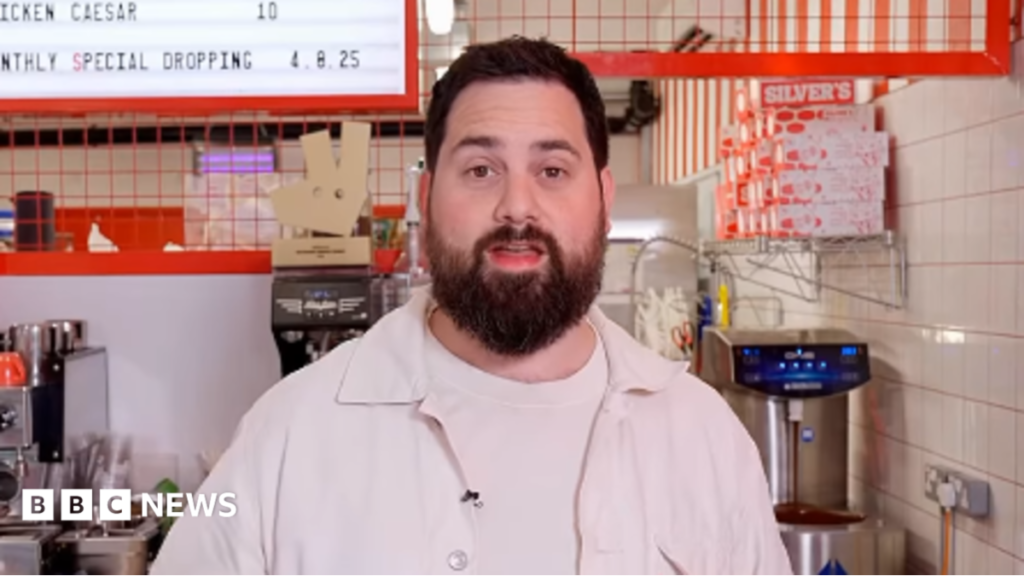 Cake freebie request from The Voice ‘abysmal’, says bakery A picture of Rich Myers standing in his shop, behind a counter. There is a coffee machine and menu in the background.