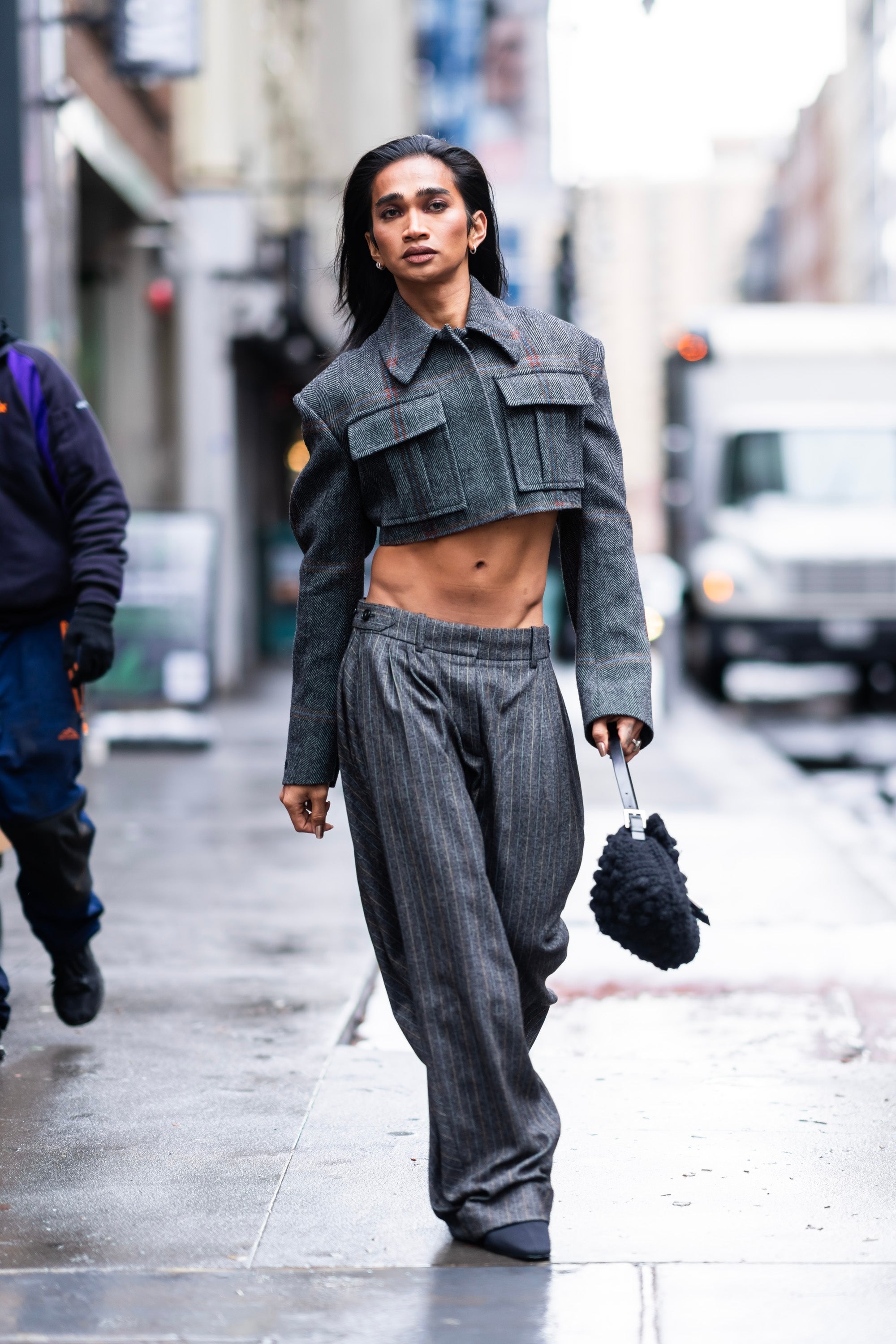 Person walking confidently on a city street wearing a stylish cropped jacket, high-waisted wide-leg pants, and carrying a textured handbag