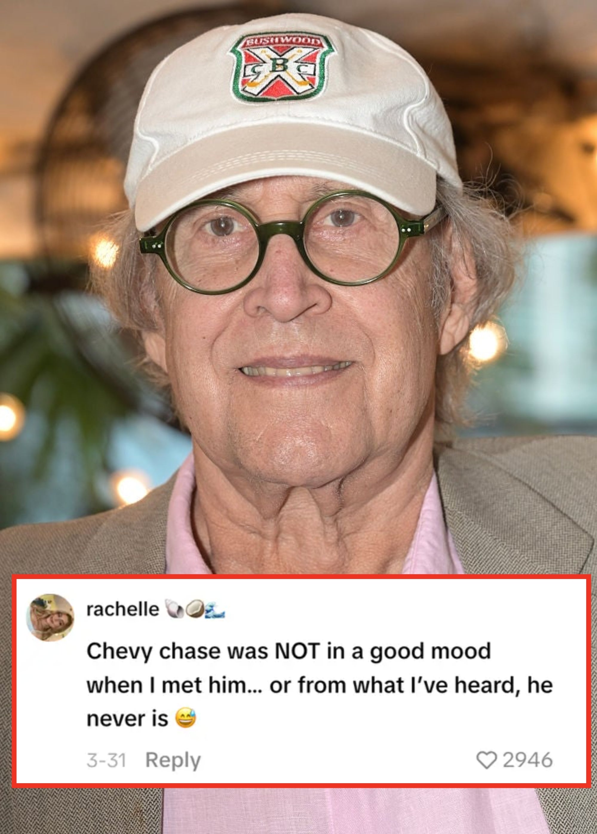 A person is wearing a pink shirt, gray blazer, and white cap with glasses, posing for a photo