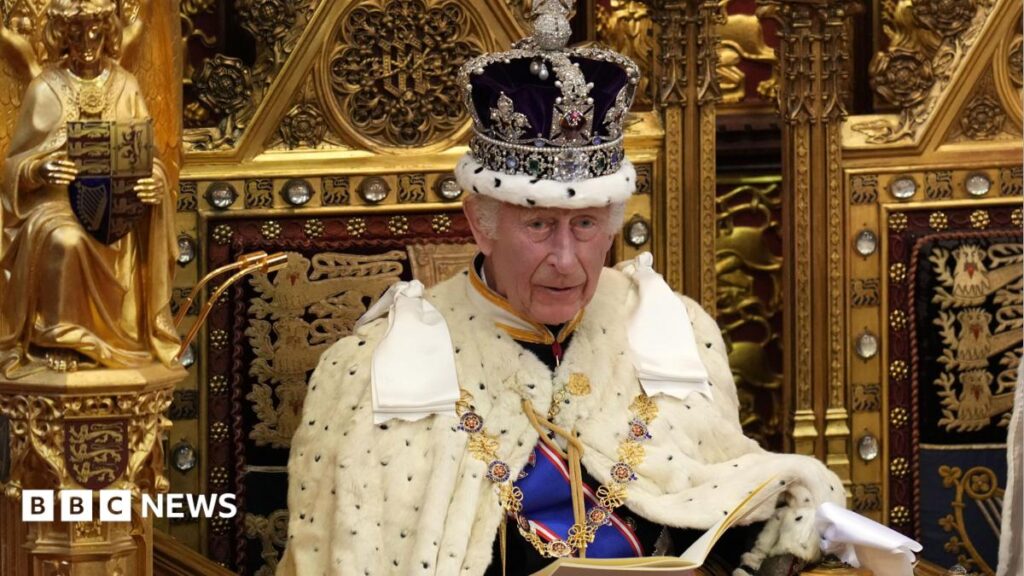 King Charles sitting on a golden throne with a crown on.