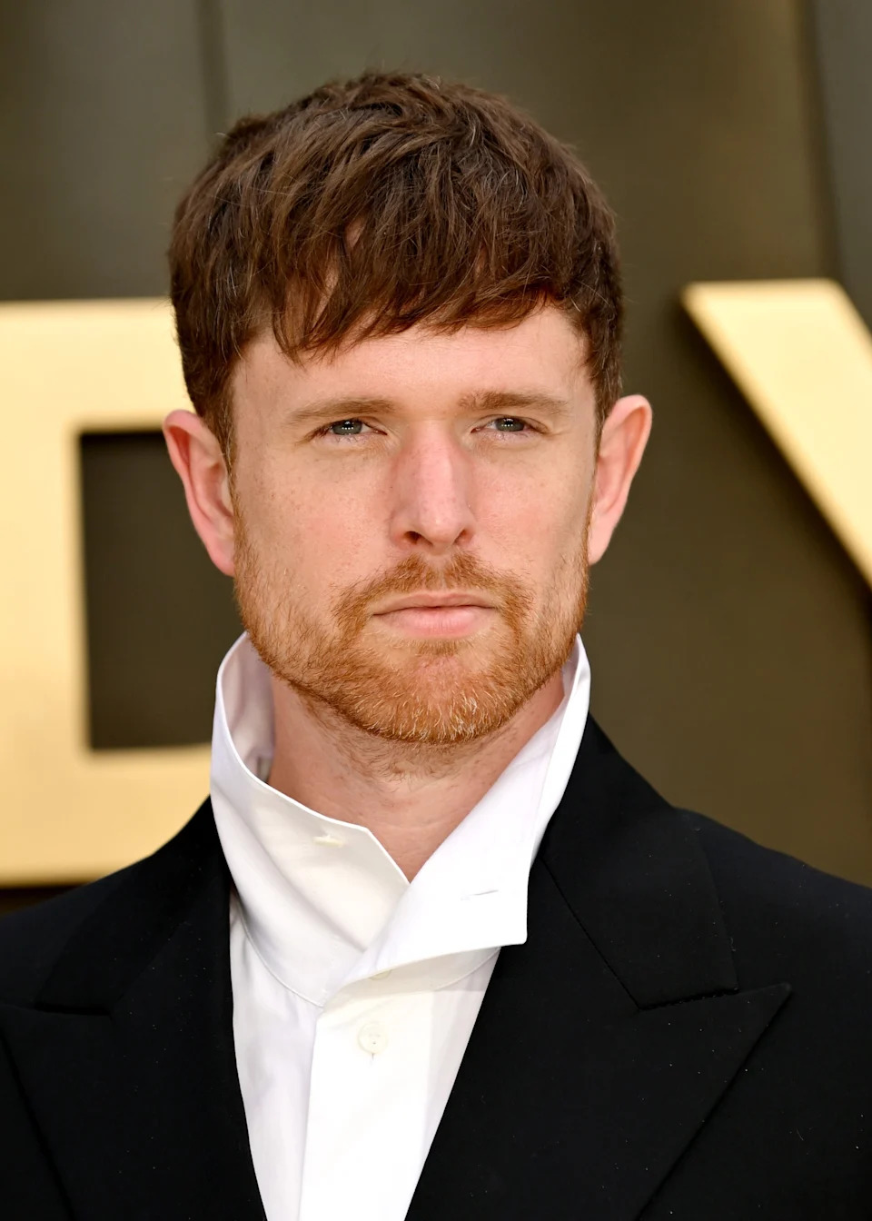 A person on the red carpet wearing a tailored black suit with a unique high-collar white shirt