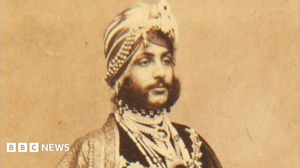 A portrait of Duleep Singh on paper that has aged over time and gone brown. He looks away from the camera and is expressionless. He has 19th Century traditional Indian headwear on as well as clothing. He also has a dark and thick beard.