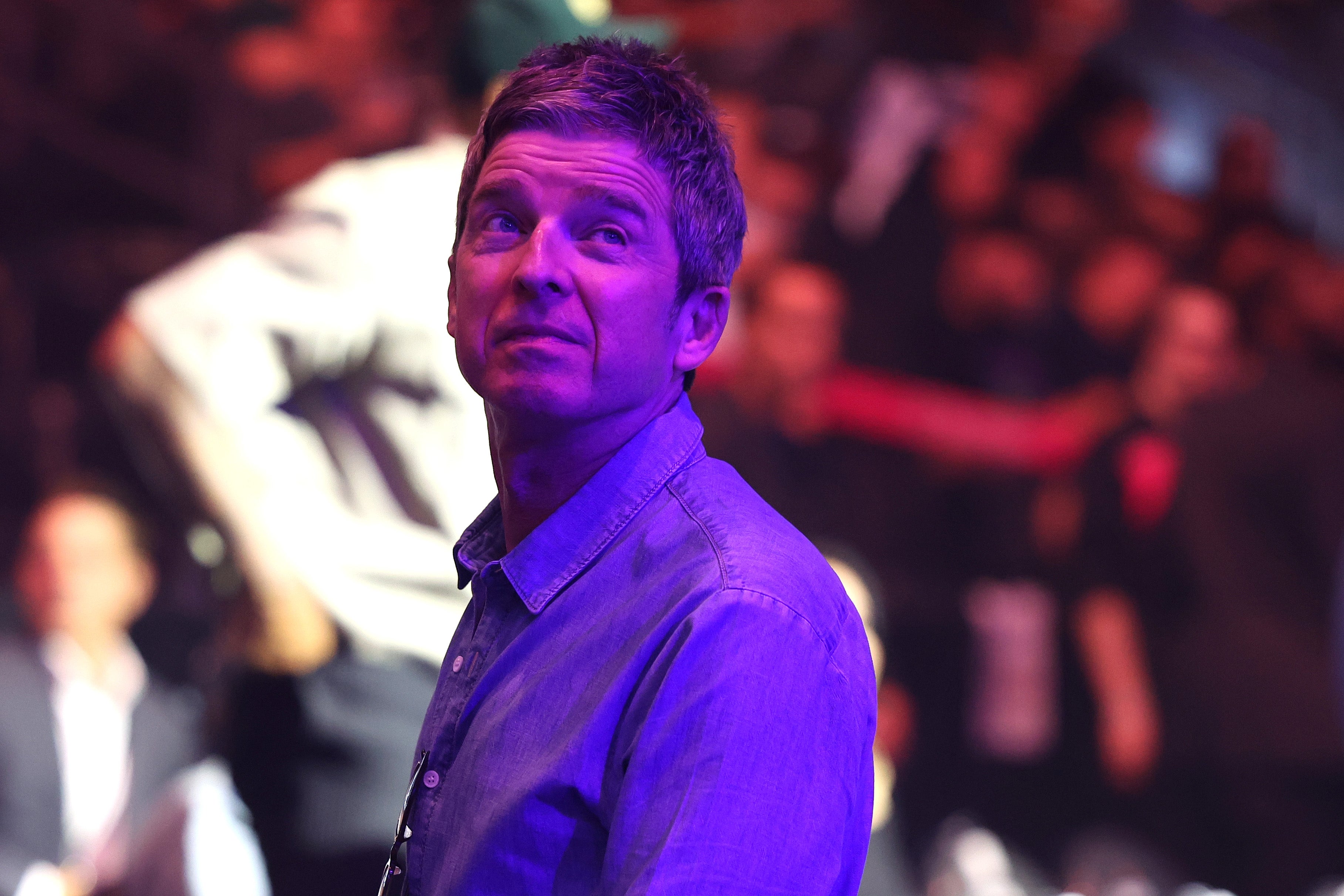 Noel Gallagher in casual attire looks up in a crowded event setting