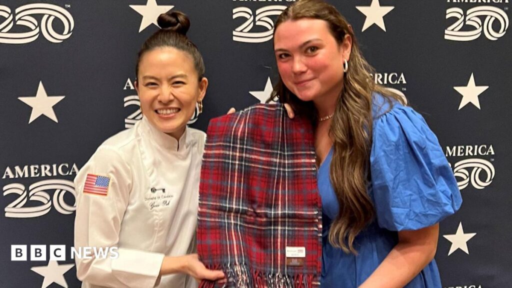 Scots designer creates tartan to mark US 250th anniversary Kaci McEwan has long brown hair and is wearing a blue dress. Grace Pak has her dark hair tied up in a bun on top of her head. She is wearing a white outfit with the US Stars and Stripes flag on the sleeve. The women are holding a scarf, which has been woven in the US 250th anniversary tartan colours of red, blue and white.